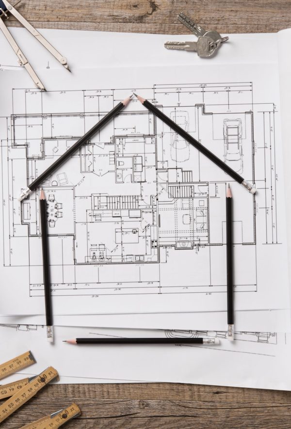 Top view of architectural blueprints, rolls and drawing instruments on the worktable. Shape of house with black pencils on a project house. Architectural drawings with house keys on wooden table, new home concept.