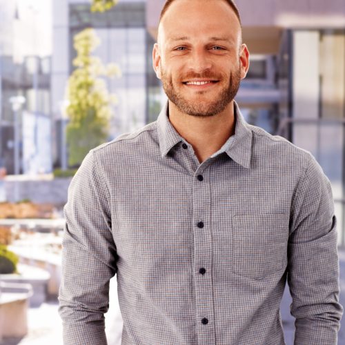 Outdoor photo of happy young man smiling, looking at camera.