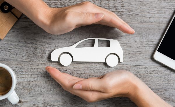 Hands protecting icon of car over wooden table. Top view of hands showing gesture of protecting car. Car insurance and automotive business concept.
