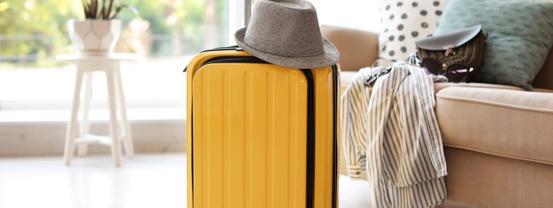 Bright yellow suitcase packed for journey and hat at home